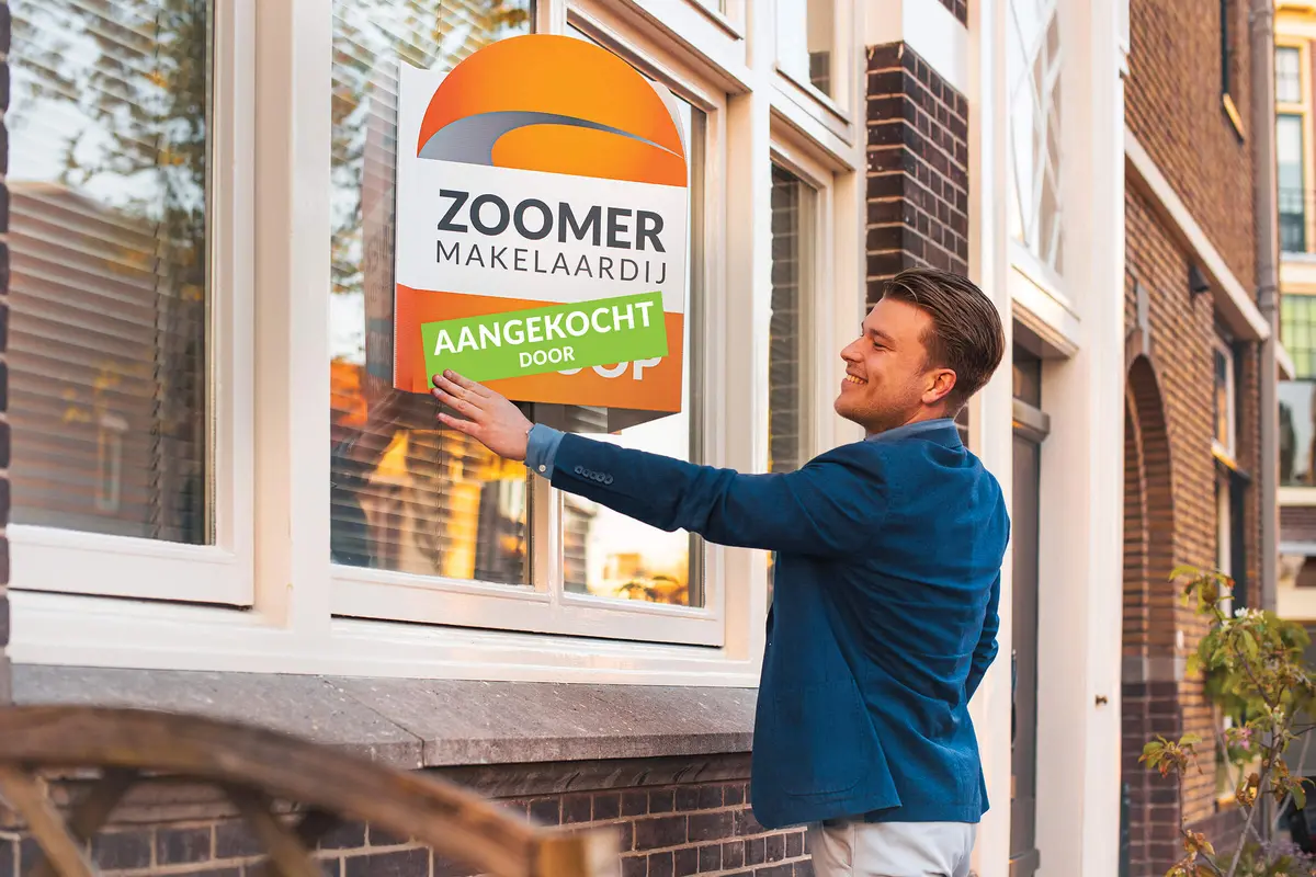 Makelaar hangt een aangekocht-bord op bij een woning
