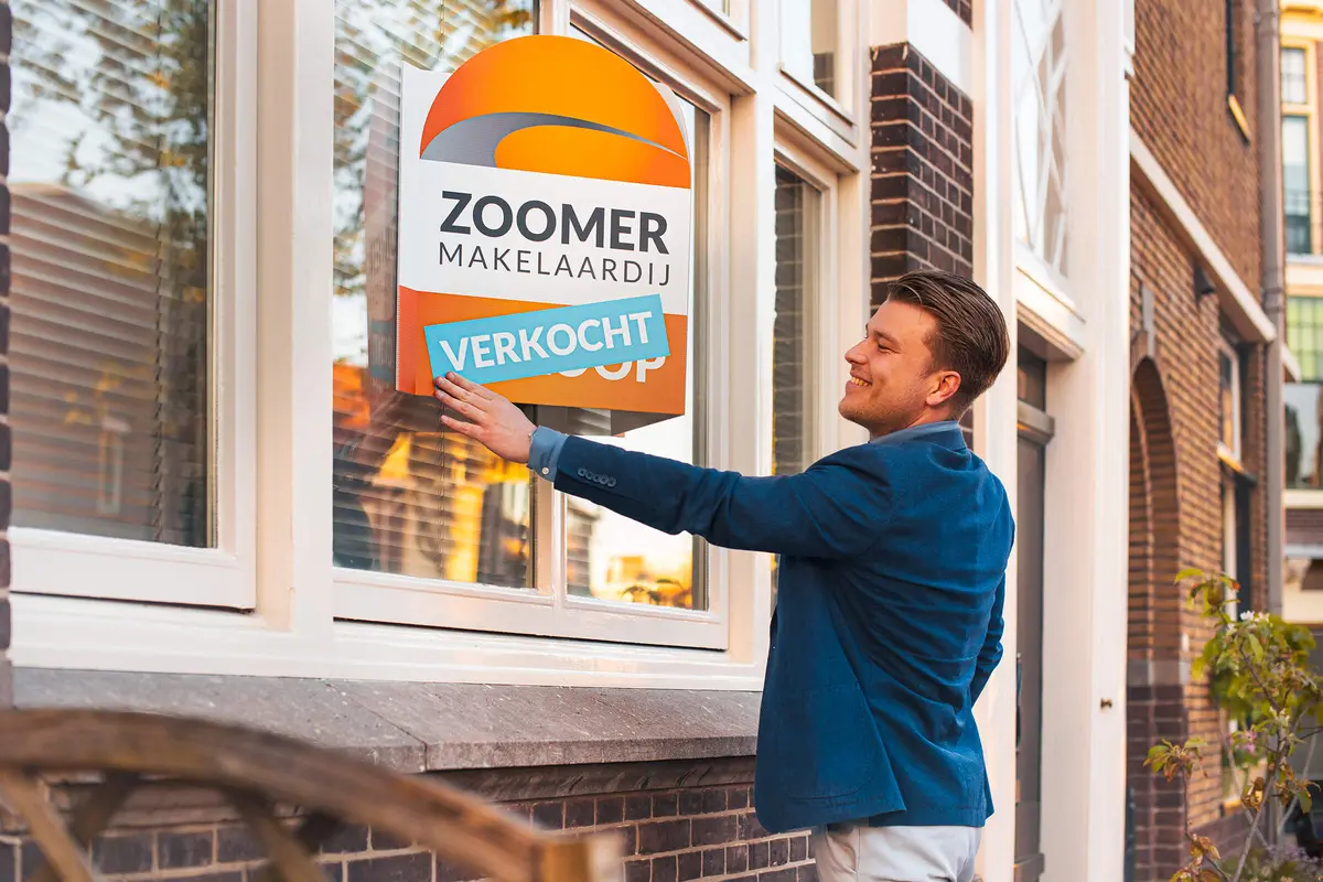 Makelaar hangt een verkocht-bord op bij een woning in Dordrecht